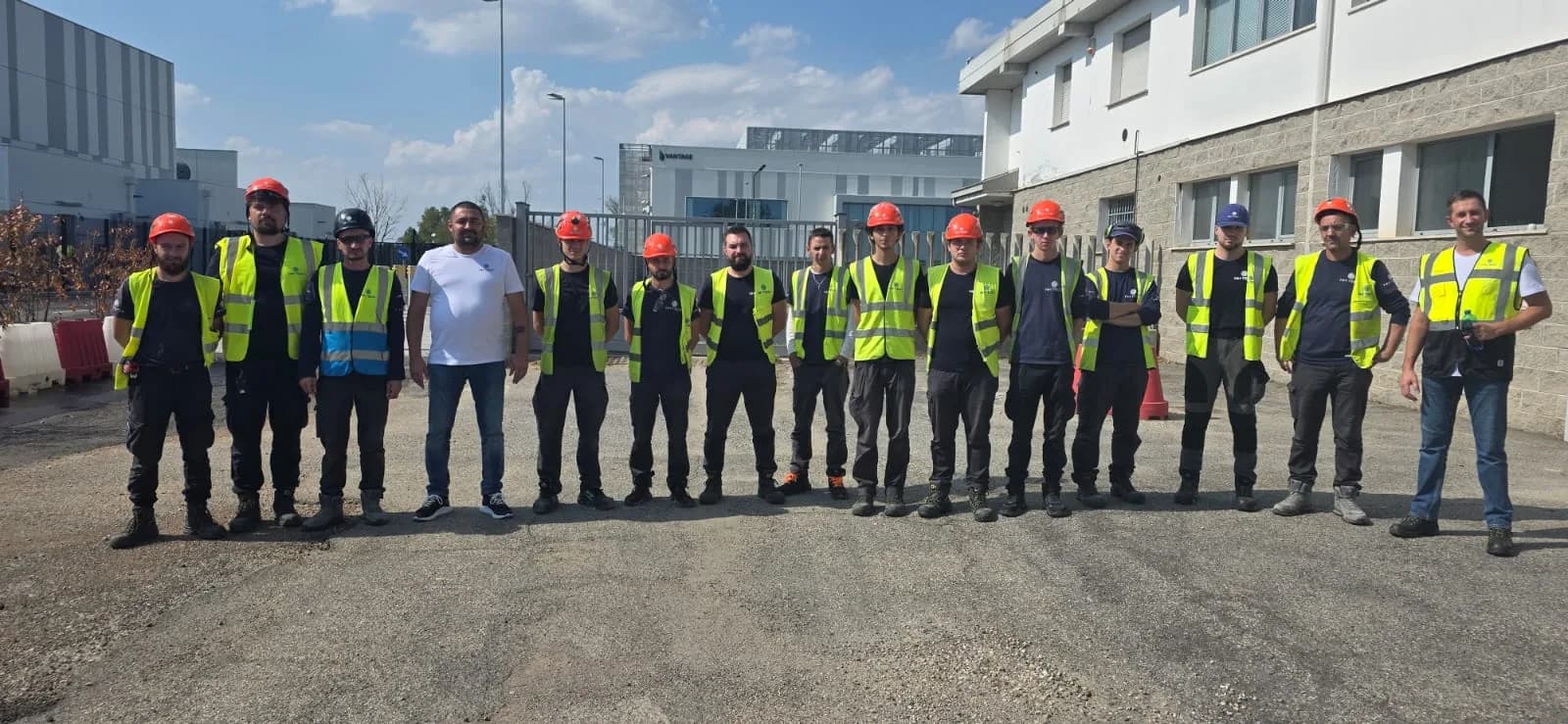 A group of NH TECH technicians in hi-vis vests and red helmets standing in a row outside a data centre building