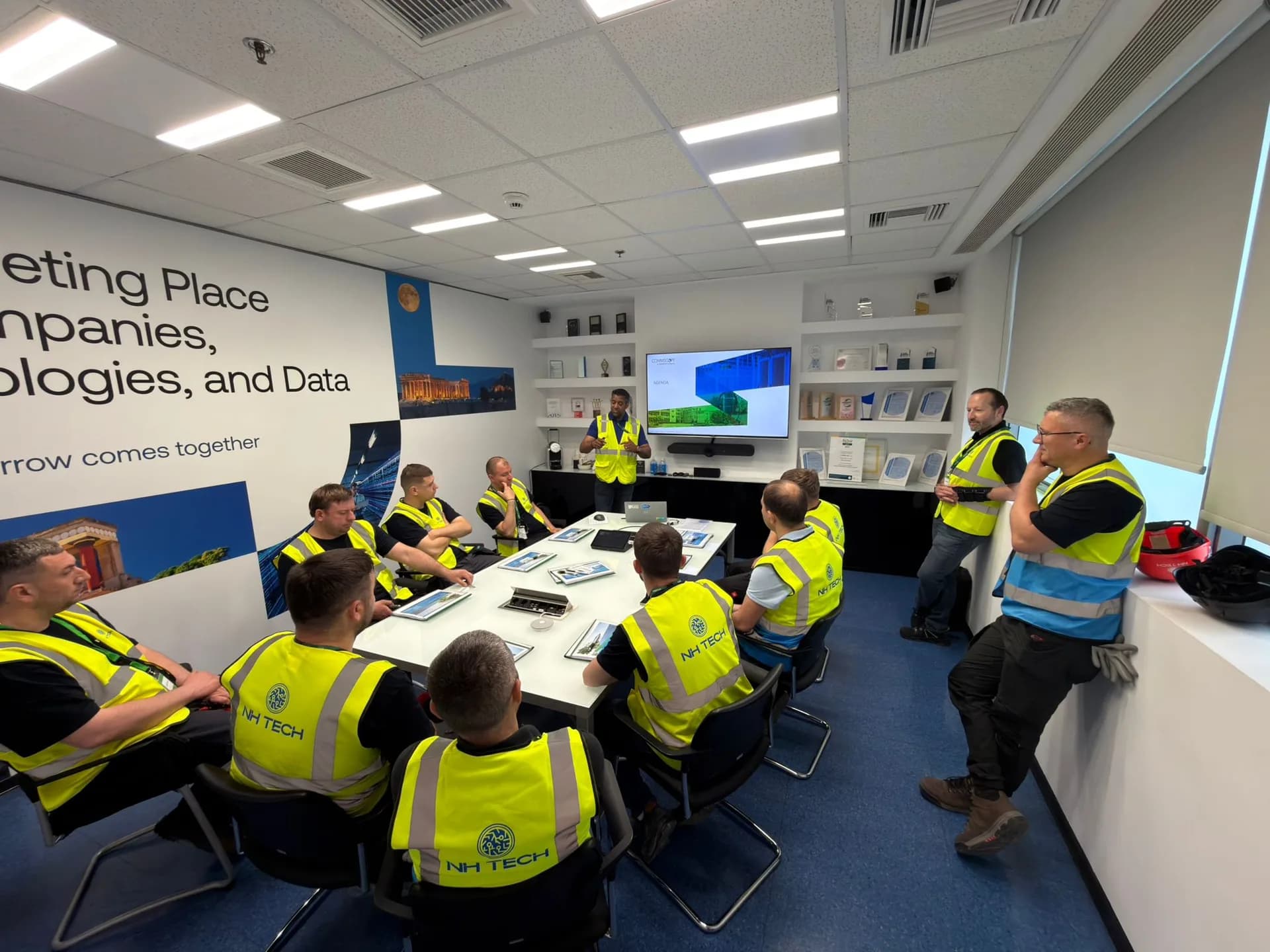 NH TECH technicians in hi-vis vests seated around a conference table during a training presentation