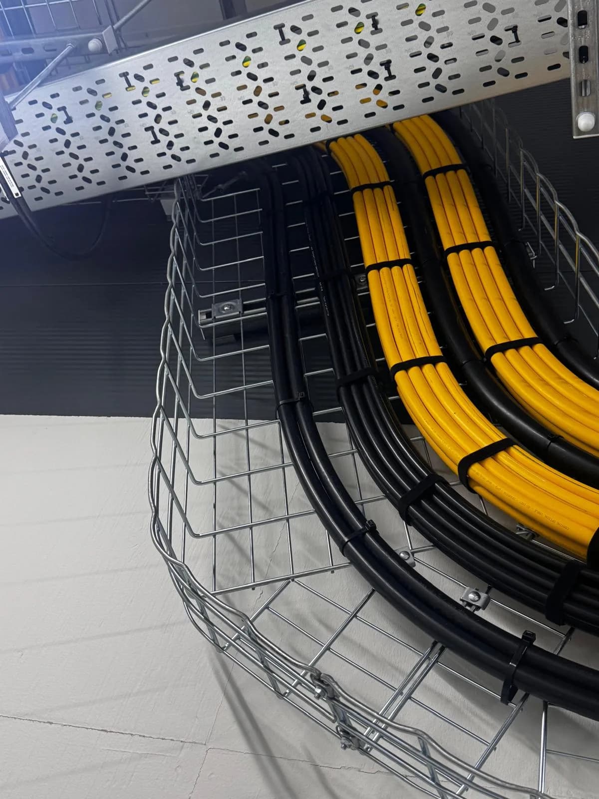 Yellow and black cables strapped along a curved wire basket tray under a perforated cable ladder