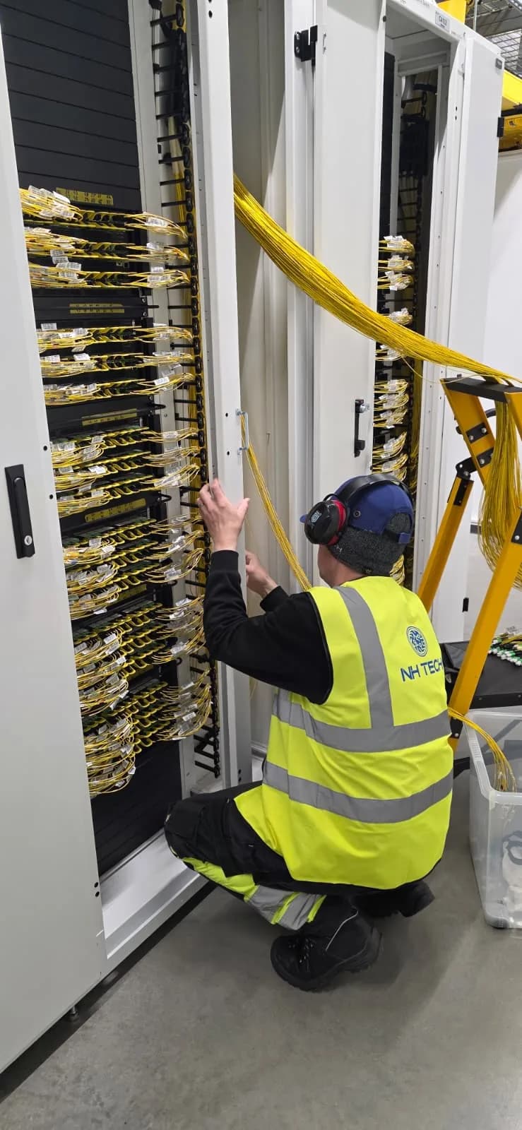 A technician crouching at an open cabinet, patching yellow fibre cords into high-density panels