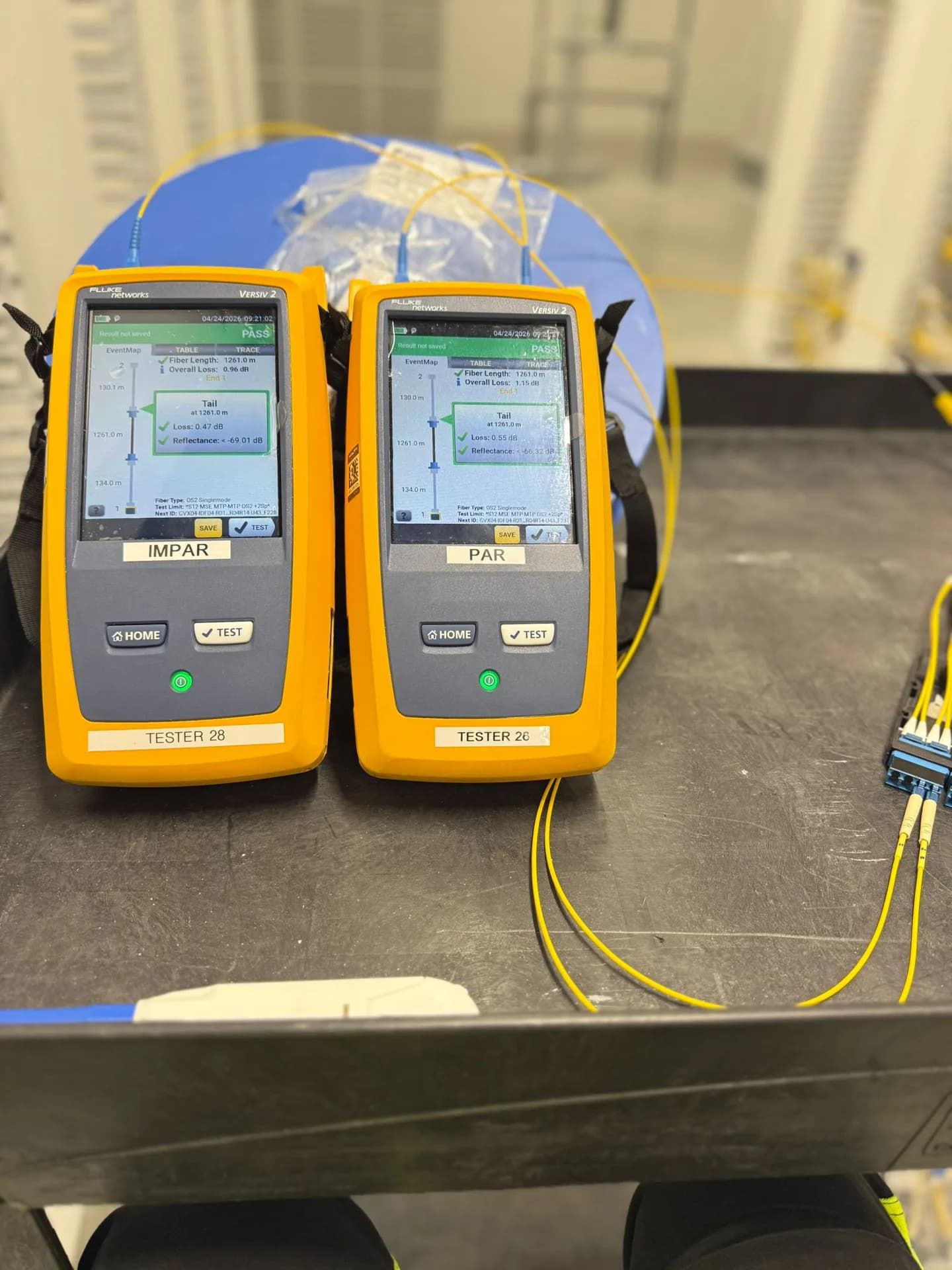 Two Fluke Versiv fibre testers on a cart, each screen showing a PASS result for a single-mode link
