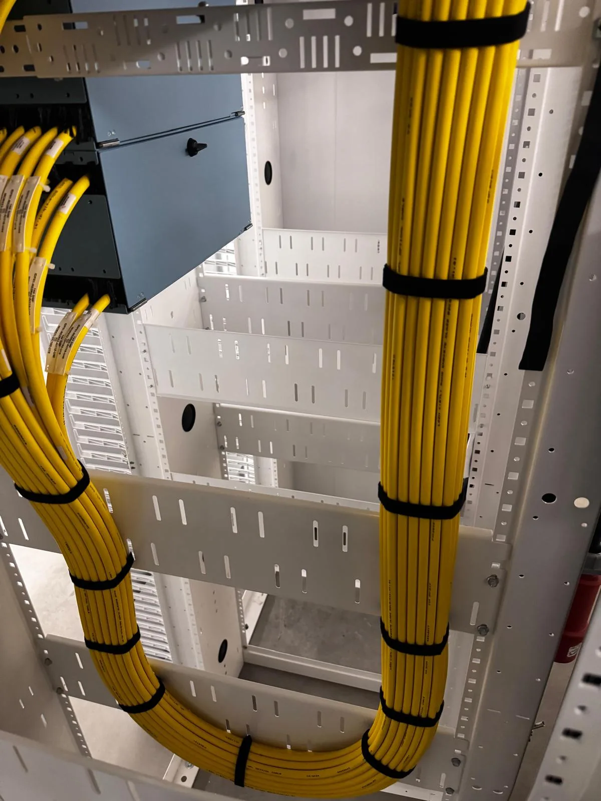 Bundles of yellow fibre trunk cables neatly looped and strapped inside a white rack frame